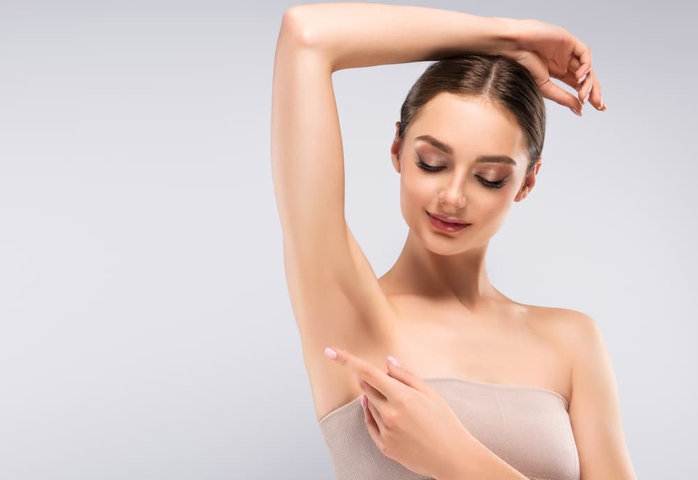 Woman with smooth underarm skin pointing at her underarm, showing results of a clean and professional waxing treatment.