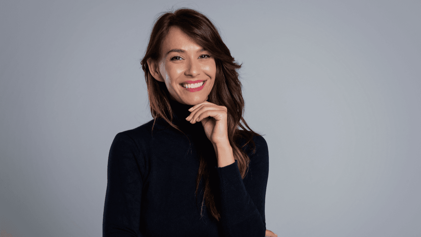 A confident, smiling woman with rich brunette hair and flawless colour poses against a neutral background. Her hair is smooth and evenly toned with no visible regrowth, reflecting the results of expert grey coverage and root touch-up services available at Honeys Hair & Beauty in Taunton.