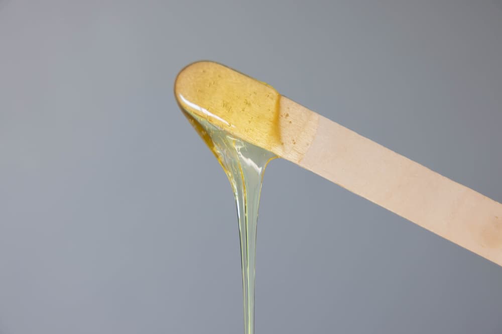 Close-up of warm wax dripping from a wooden spatula, highlighting the importance of avoiding double dipping during professional waxing treatments.